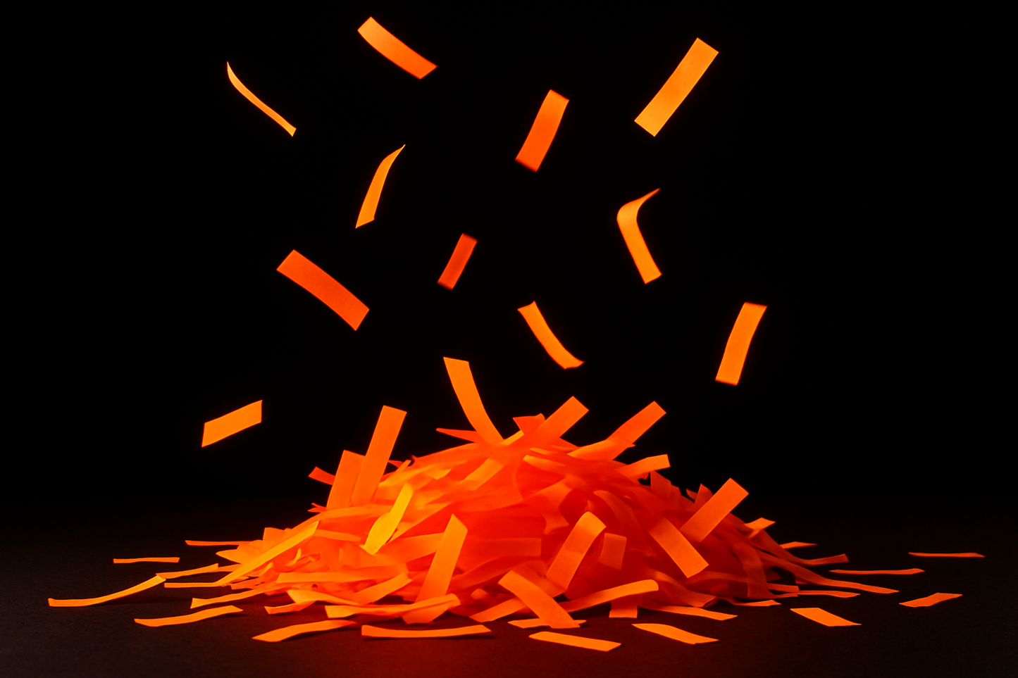 neon orange confetti strips in a pile with some floating with dark background